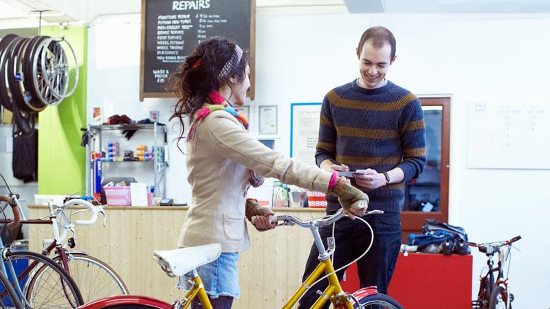 A woman standing happily with her her bicycle in a local bike shop.